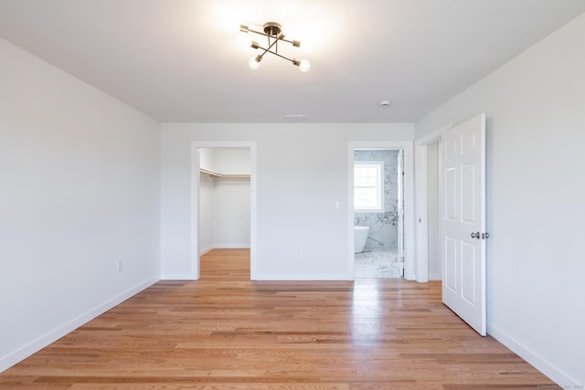 unfurnished bedroom with a walk in closet, light wood-type flooring, a closet, baseboards, and ensuite bathroom