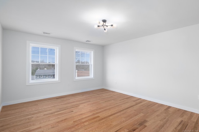 unfurnished room with baseboards, a chandelier, light wood-style floors, and visible vents