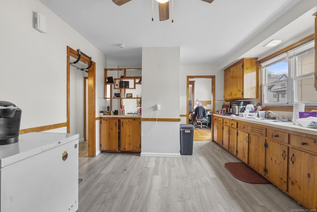 kitchen with brown cabinets, fridge, ceiling fan, light countertops, and light wood-type flooring