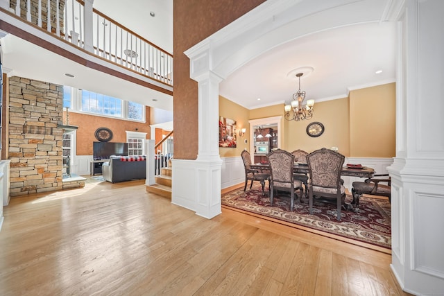 dining room featuring stairs, wainscoting, a chandelier, wood-type flooring, and decorative columns