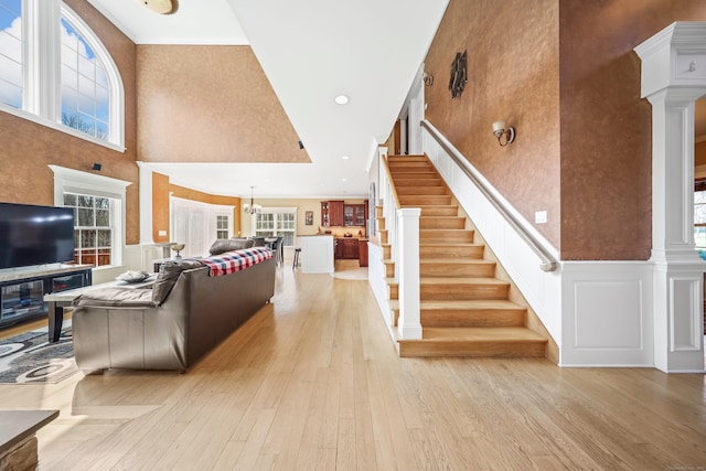 living area featuring light wood-style flooring, a wealth of natural light, a towering ceiling, and stairs