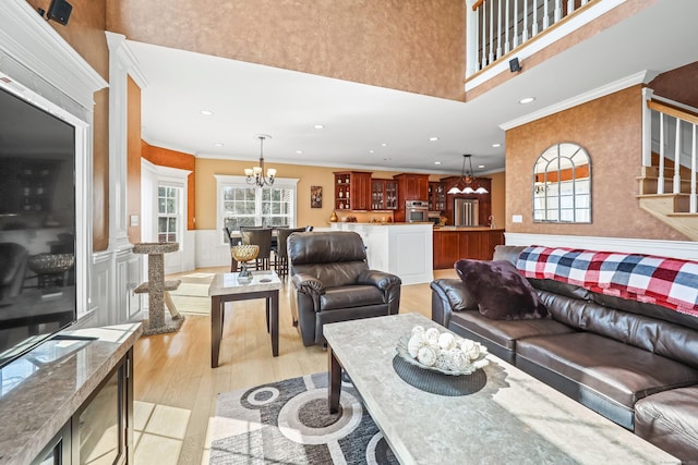 living room with stairway, a high ceiling, light wood finished floors, ornamental molding, and a chandelier