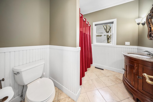 bathroom featuring a wainscoted wall, tile patterned floors, visible vents, toilet, and ornamental molding