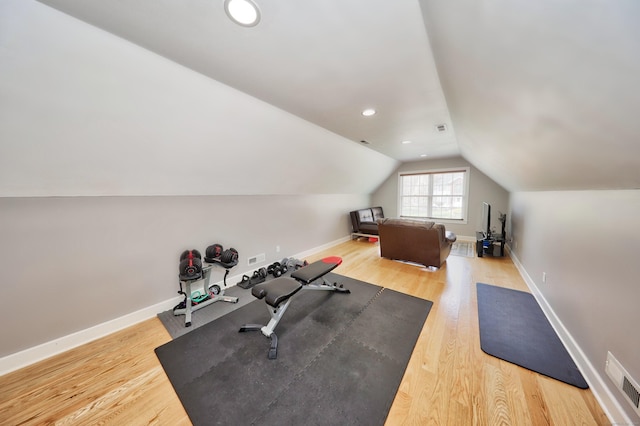 exercise room with visible vents, baseboards, vaulted ceiling, and wood finished floors