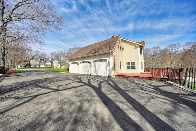 view of property exterior with a deck, a garage, aphalt driveway, and fence