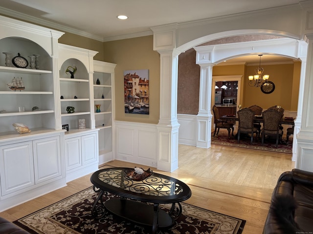 living room with a chandelier, light wood finished floors, arched walkways, and decorative columns