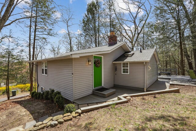 exterior space with a shingled roof, a chimney, and a deck