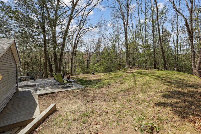 view of yard with a wooden deck, a wooded view, and a patio