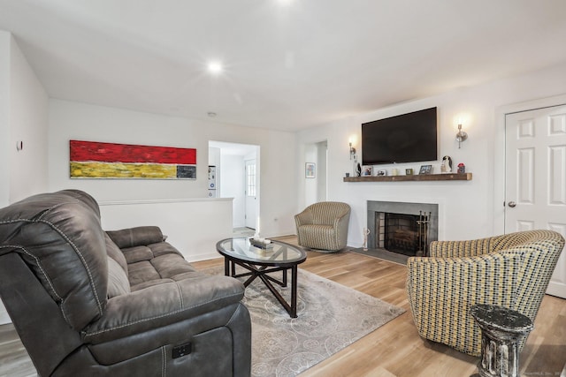 living area featuring a fireplace with flush hearth, wood finished floors, and baseboards