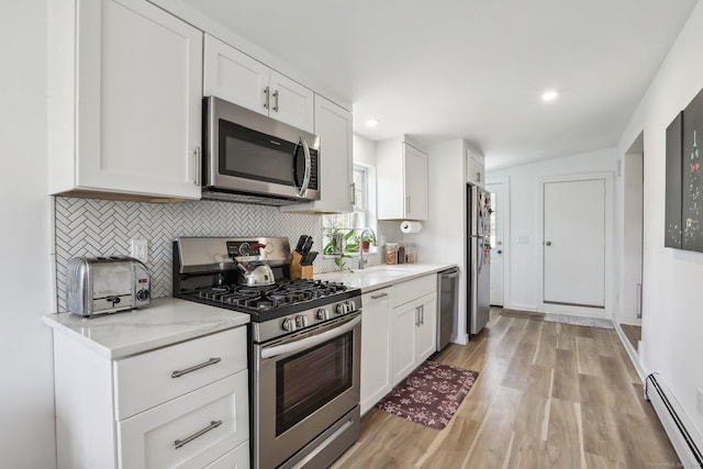kitchen with a baseboard radiator, tasteful backsplash, a sink, light wood finished floors, and appliances with stainless steel finishes