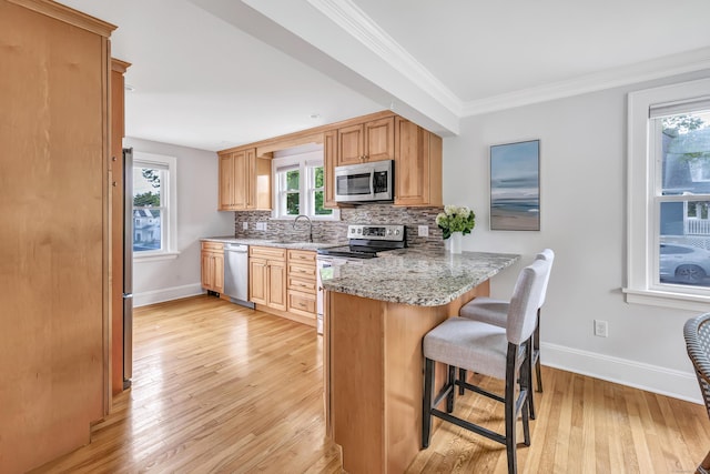 435 Lenox Rd, Fairfield, CT 06825 - kitchen with appliances with stainless steel finishes, a kitchen bar, baseboards, light wood-style flooring, and crown molding