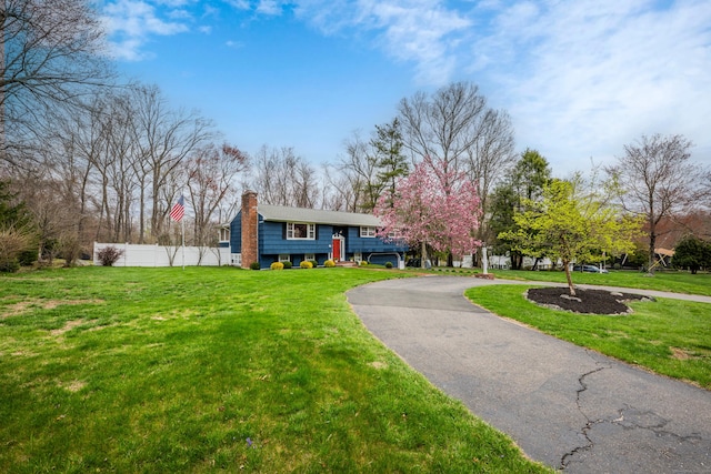 raised ranch with a front lawn, aphalt driveway, fence, and a chimney