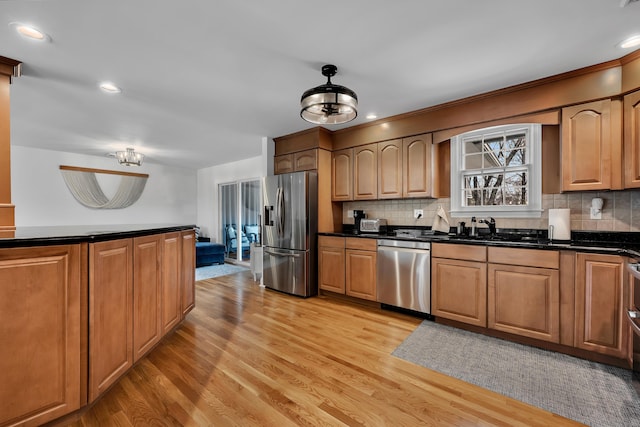 kitchen with a sink, light wood finished floors, appliances with stainless steel finishes, and decorative backsplash