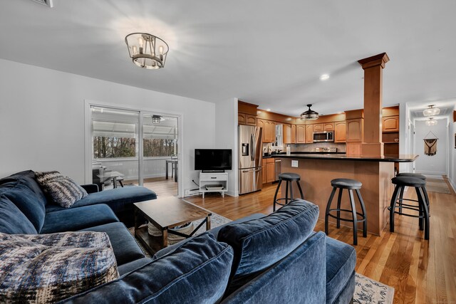 living area with ornate columns, baseboards, and light wood finished floors
