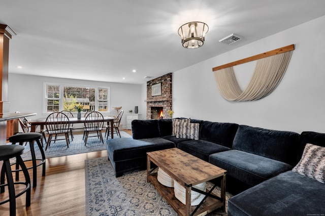 living area featuring a notable chandelier, a brick fireplace, recessed lighting, wood finished floors, and visible vents