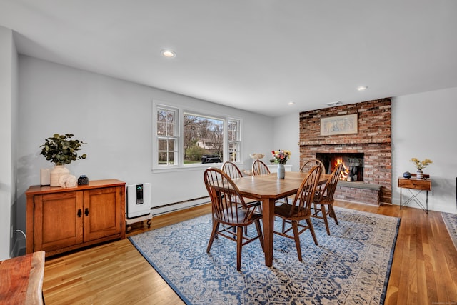dining area featuring recessed lighting, a baseboard radiator, light wood finished floors, and a fireplace