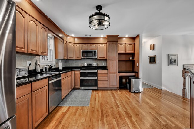 kitchen with backsplash, dark countertops, appliances with stainless steel finishes, baseboards, and light wood finished floors