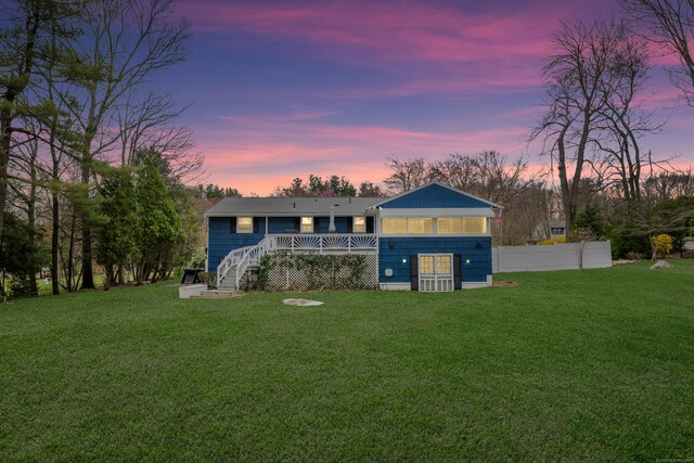 back of house at dusk with fence, a deck, a yard, and stairway