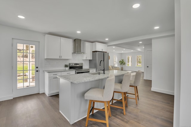 kitchen featuring appliances with stainless steel finishes, wall chimney range hood, recessed lighting, plenty of natural light, and white cabinetry