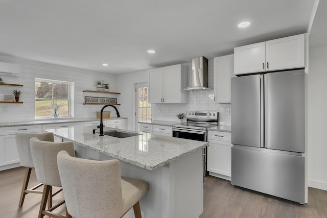 kitchen featuring stainless steel appliances, open shelves, wall chimney range hood, a sink, and tasteful backsplash