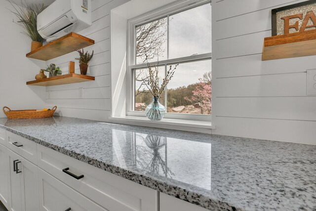 detailed view of open shelves, a wall unit AC, white cabinetry, and light stone counters