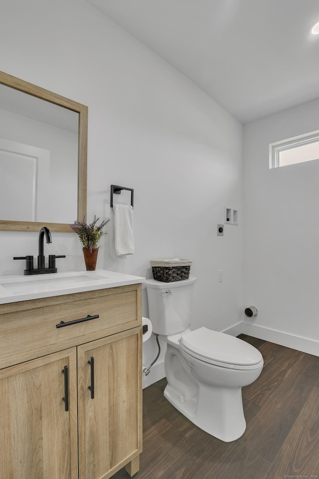 half bathroom with toilet, wood finished floors, vanity, and baseboards