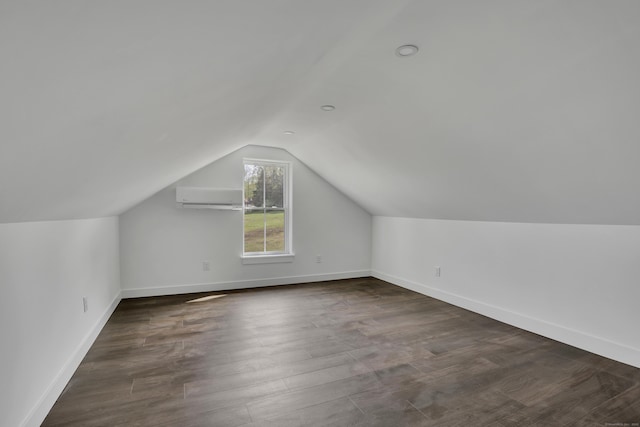additional living space featuring a wall unit AC, lofted ceiling, dark wood-type flooring, and baseboards