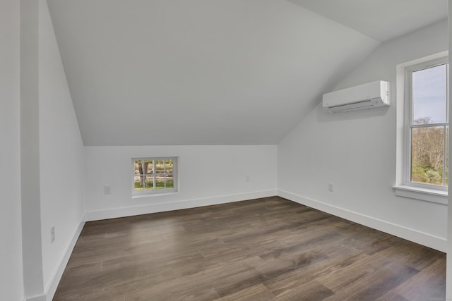 bonus room with vaulted ceiling, an AC wall unit, healthy amount of natural light, baseboards, and dark wood-style flooring