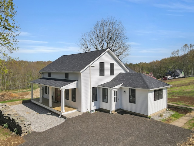 view of front of home featuring covered porch, roof with shingles, a view of trees, and gravel driveway