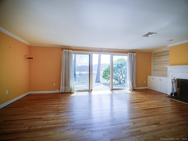 unfurnished living room featuring visible vents, wood finished floors, baseboards, and crown molding