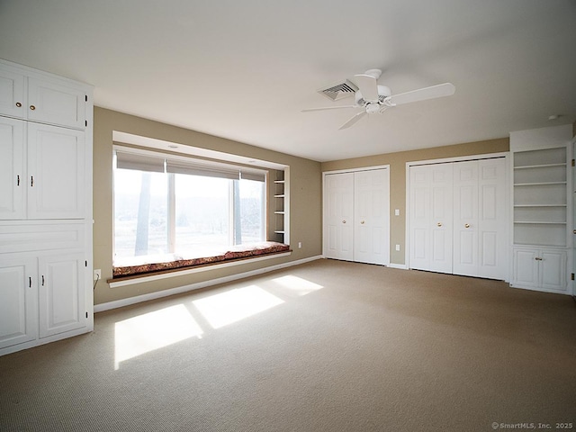 unfurnished bedroom featuring multiple closets, visible vents, a ceiling fan, baseboards, and carpet flooring