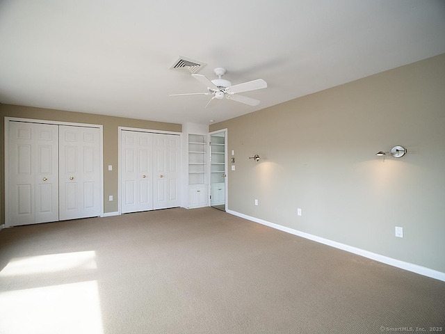 unfurnished bedroom featuring visible vents, baseboards, carpet, and two closets