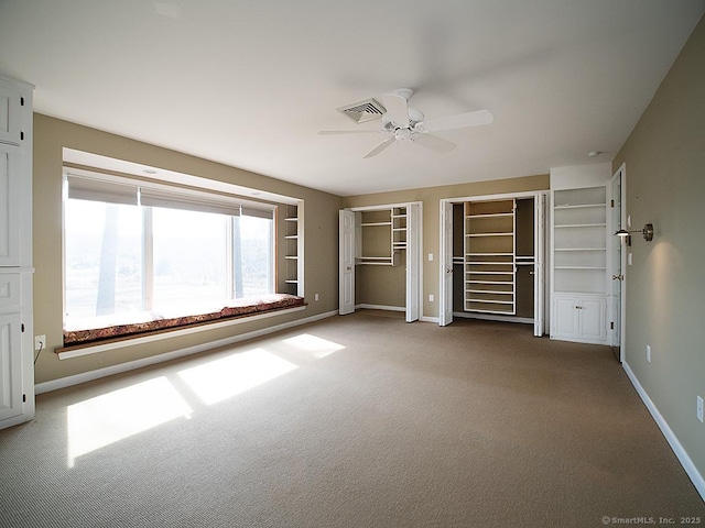unfurnished bedroom featuring visible vents, baseboards, ceiling fan, multiple closets, and carpet floors