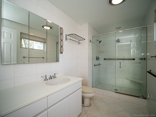 bathroom featuring tile patterned floors, toilet, vanity, tile walls, and a stall shower