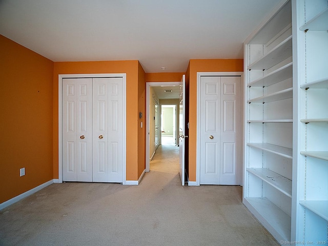 unfurnished bedroom featuring light carpet, multiple closets, and baseboards