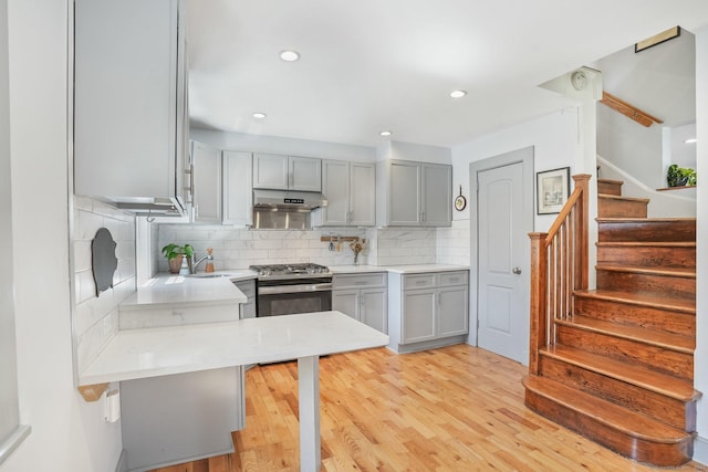 kitchen featuring gray cabinetry, gas range, under cabinet range hood, and decorative backsplash