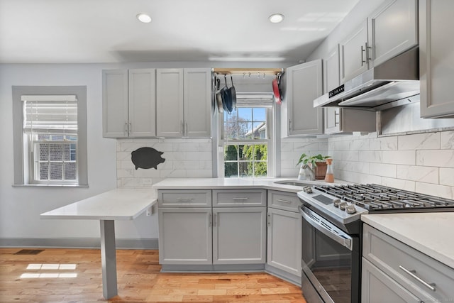 kitchen featuring gray cabinets, under cabinet range hood, light countertops, light wood-type flooring, and stainless steel gas range