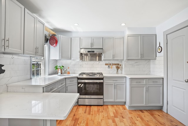 kitchen featuring a sink, stainless steel gas range oven, decorative backsplash, and gray cabinets