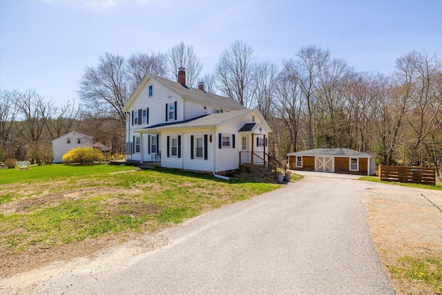 view of property exterior featuring a chimney, a lawn, fence, an outdoor structure, and aphalt driveway