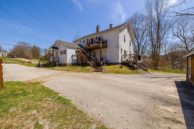 rear view of property featuring a chimney, aphalt driveway, stairway, and a deck