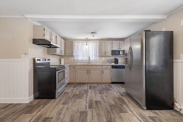 kitchen featuring a sink, a wainscoted wall, stainless steel appliances, wood finished floors, and under cabinet range hood