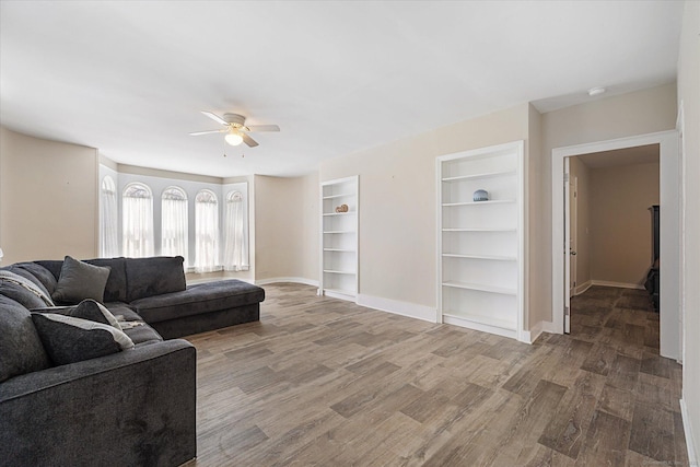 living room featuring baseboards, built in features, ceiling fan, and wood finished floors