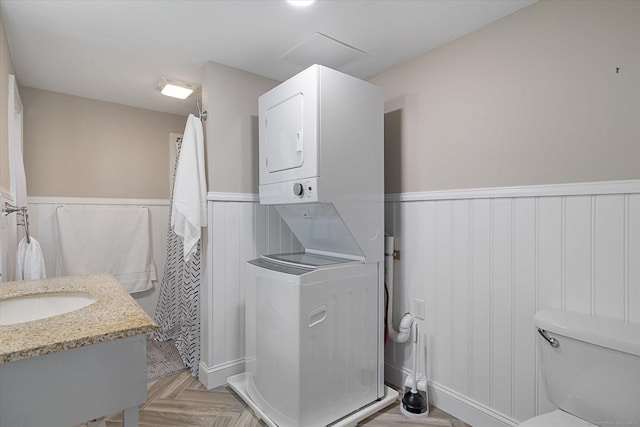 bathroom featuring stacked washing maching and dryer, a wainscoted wall, and toilet