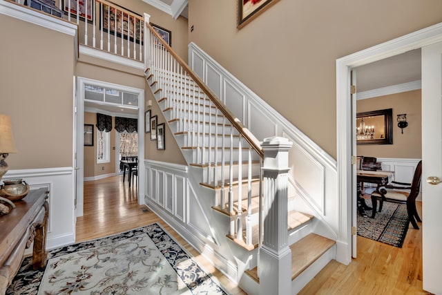 stairway with ornamental molding, wainscoting, wood finished floors, and a chandelier