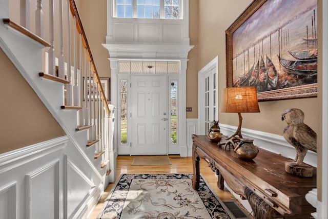 entryway featuring stairs, a high ceiling, light wood-style flooring, and a wainscoted wall