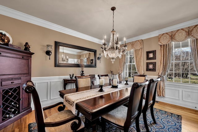 dining room featuring an inviting chandelier, ornamental molding, wainscoting, and light wood-style flooring