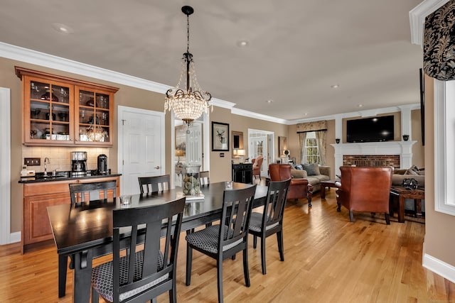 dining area featuring crown molding, a fireplace, a chandelier, baseboards, and light wood-type flooring