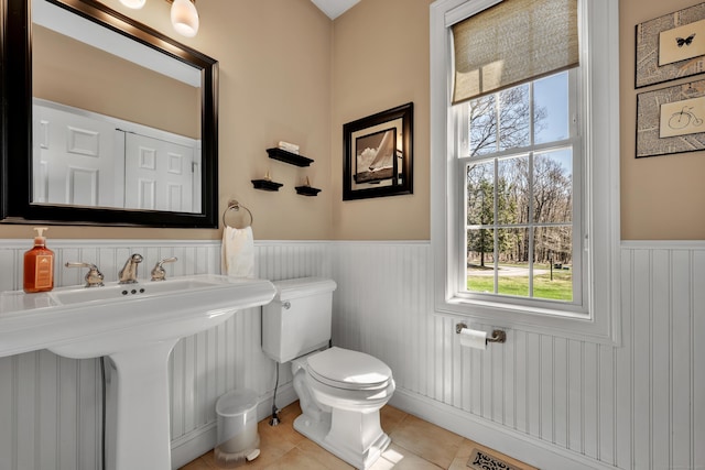 half bathroom with a healthy amount of sunlight, tile patterned flooring, wainscoting, and toilet