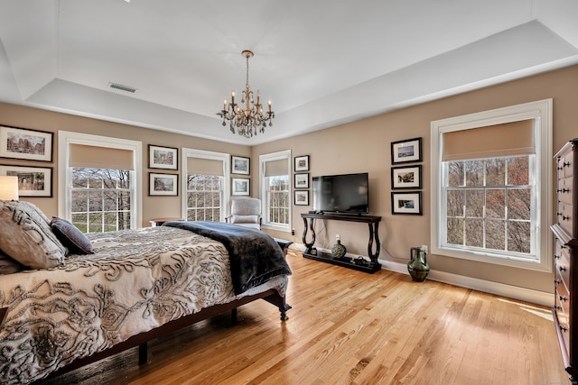 bedroom featuring a notable chandelier, light wood finished floors, baseboards, a tray ceiling, and visible vents