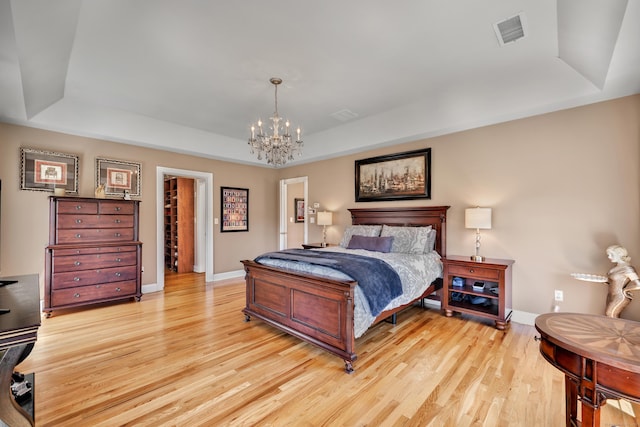 bedroom featuring a chandelier, visible vents, light wood finished floors, and a raised ceiling